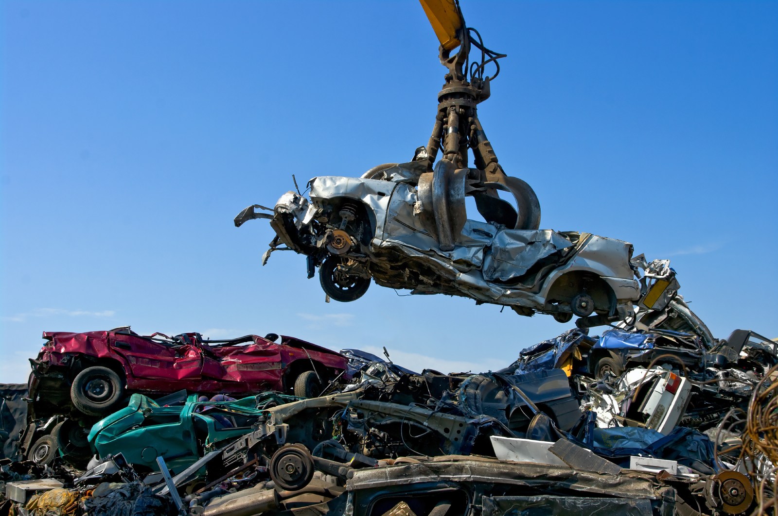 Large crane holding wrecked car over heap of scrap metal